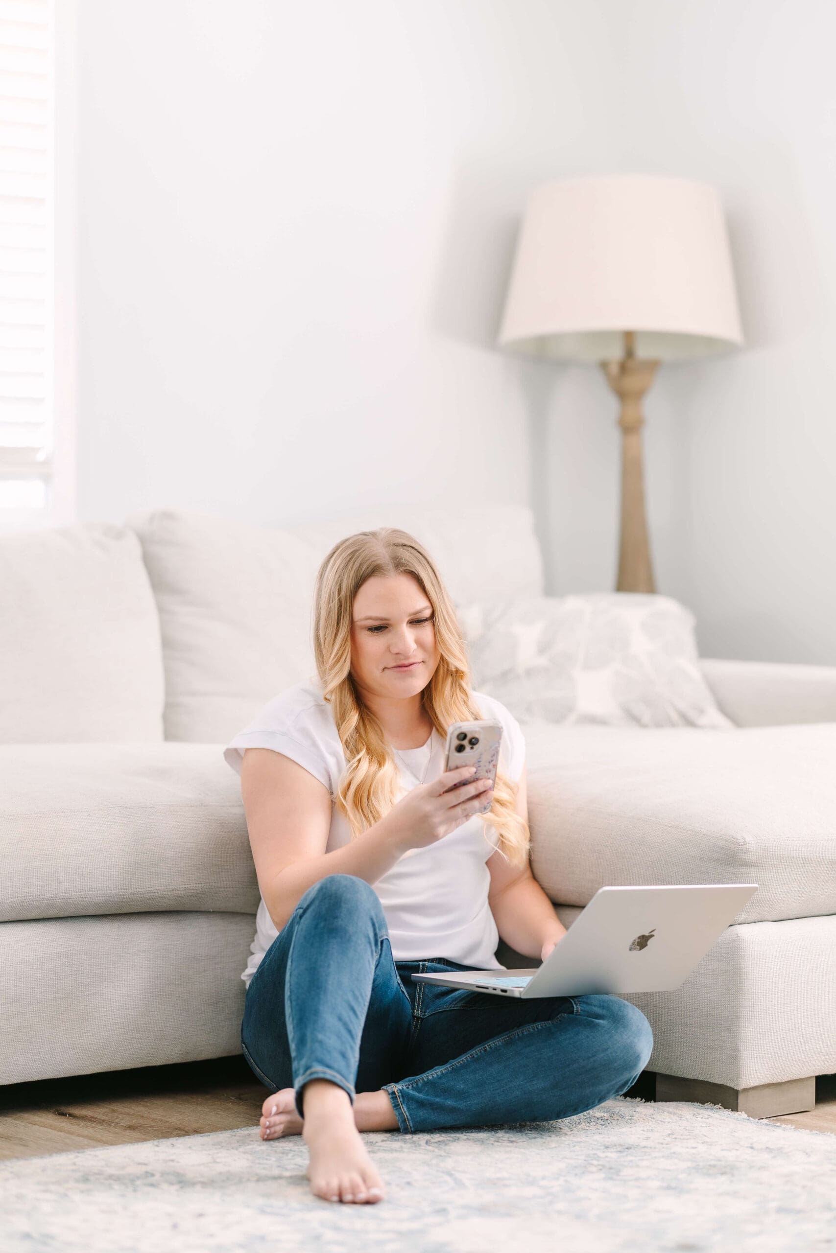 A woman sits on the floor against a couch with a laptop and phone in her hands after exploring Color Psychology in Branding