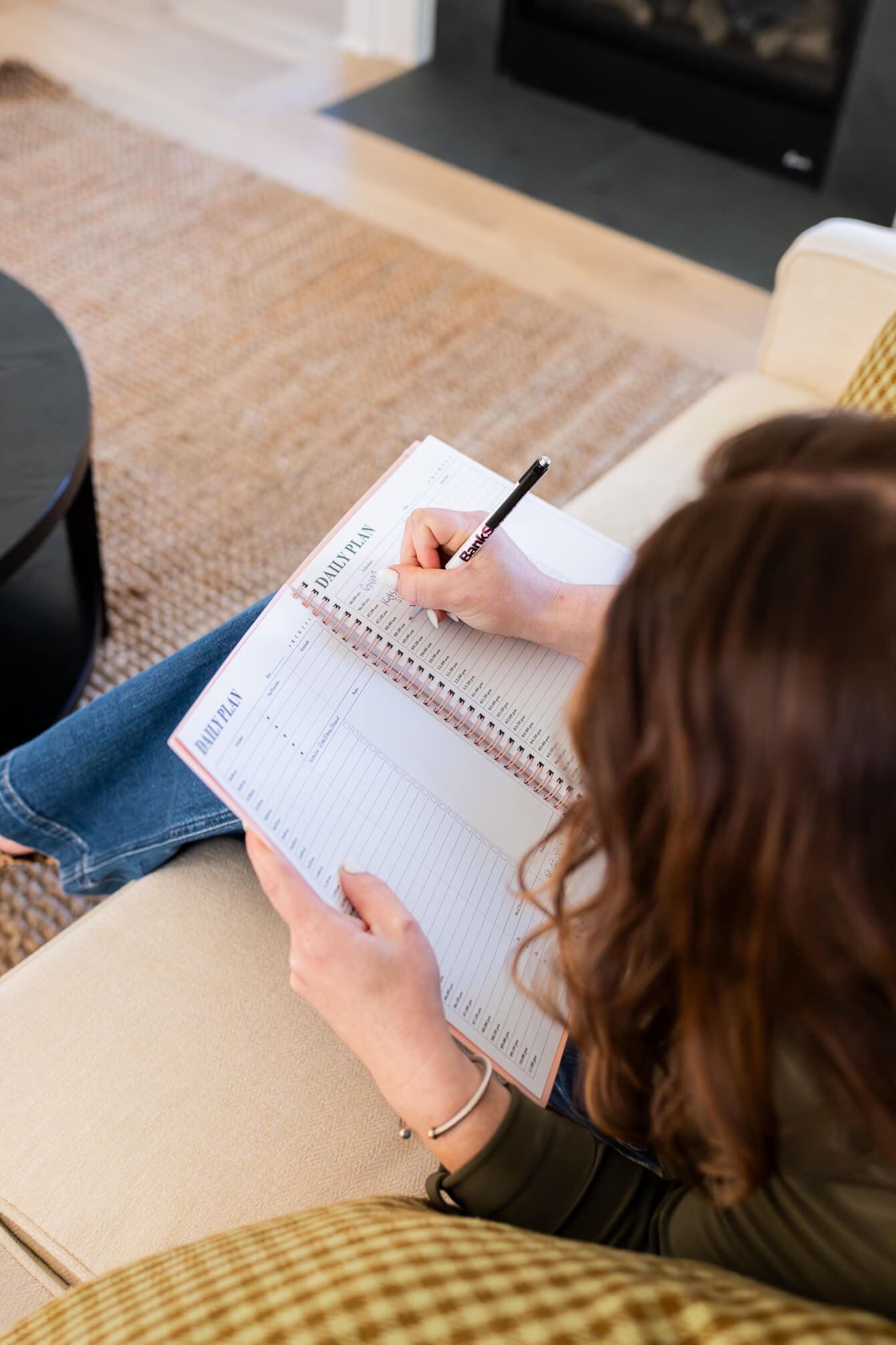 A look over a woman's shoulder as she sits on a couch making a to do list