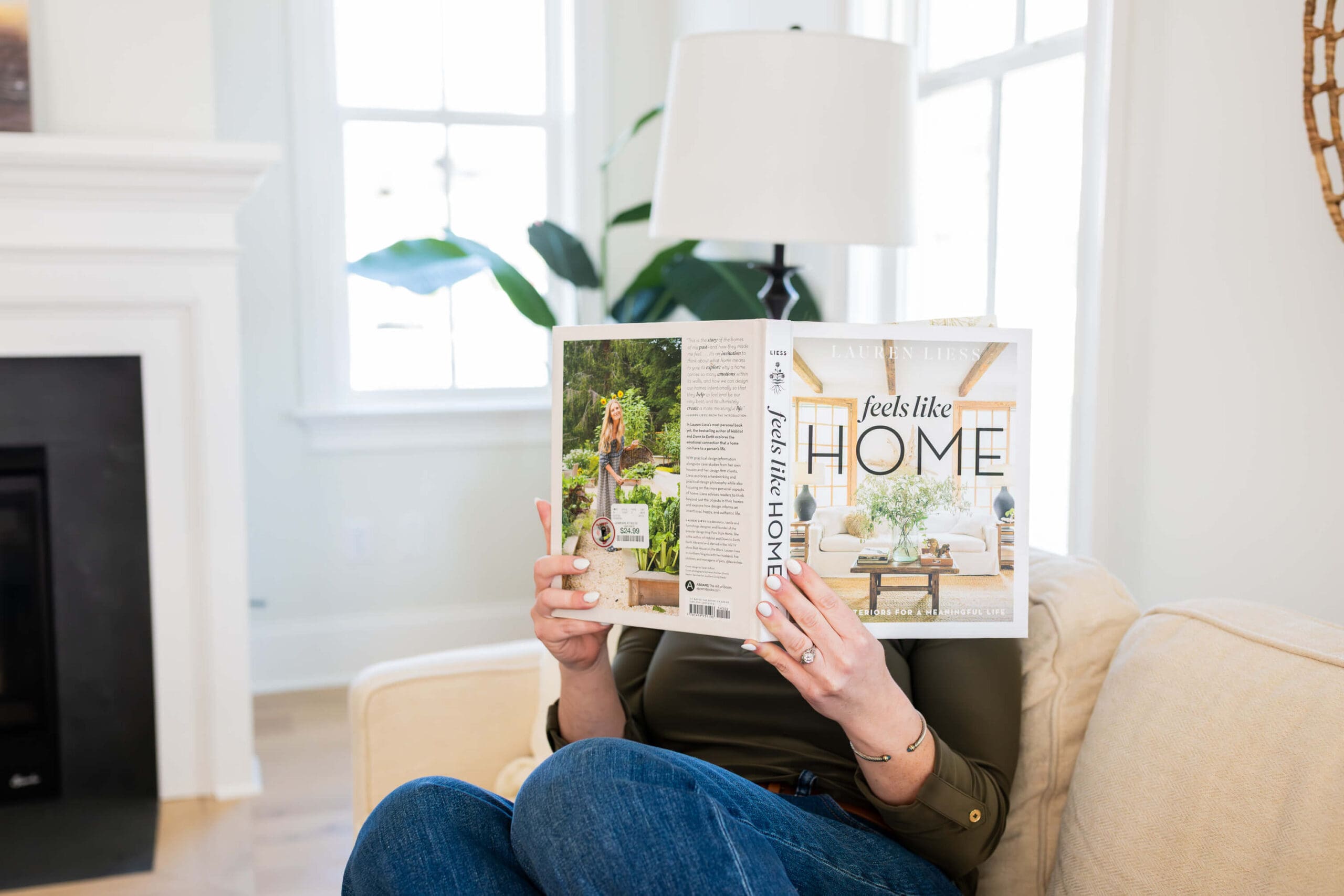 A woman reads a book about homes while sitting on a couch