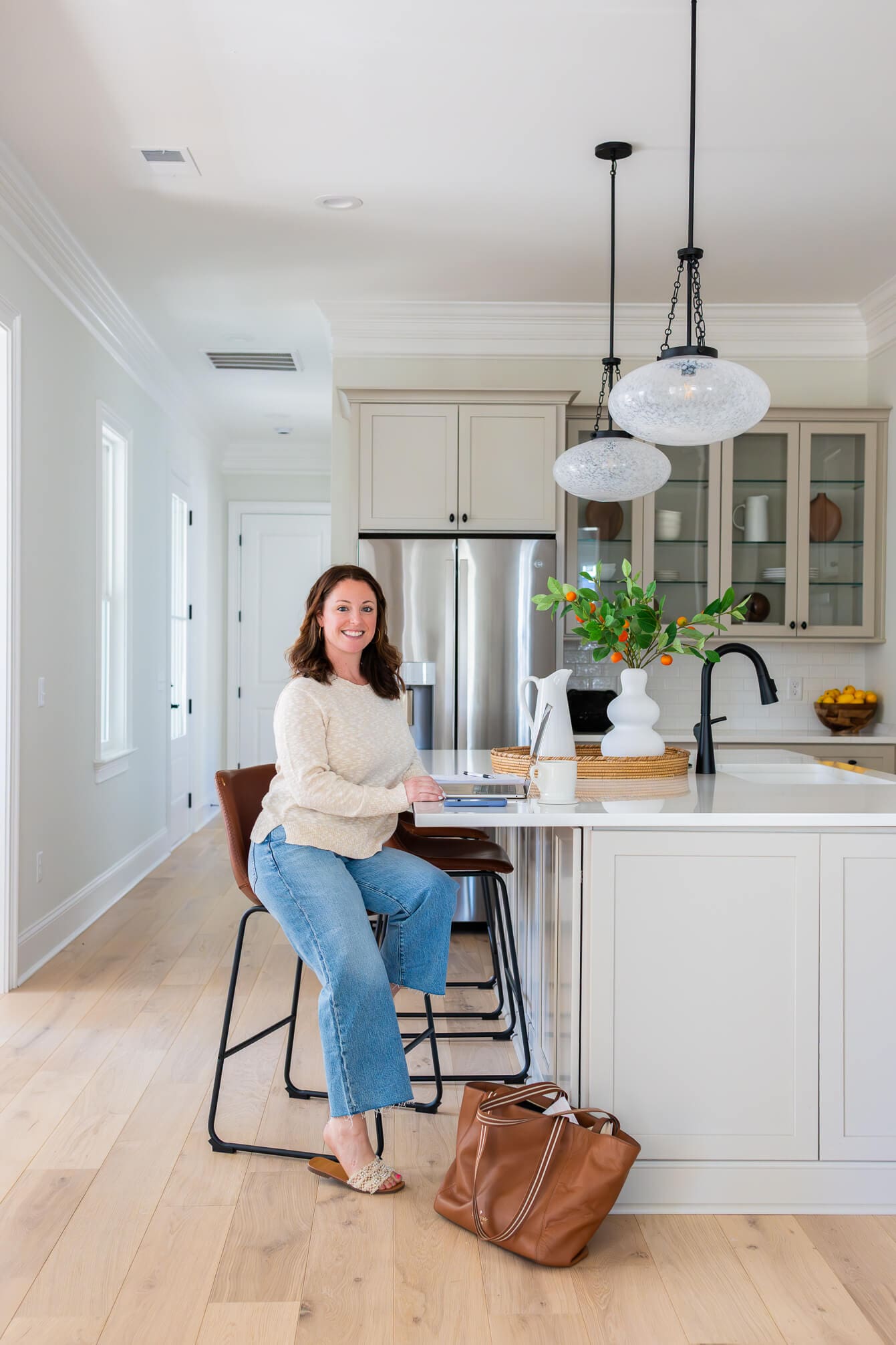 A smiling woman sitting at a kitchen island in a cream sweater and jeans with a laptop after learning How to Stand Out in a Saturated Market