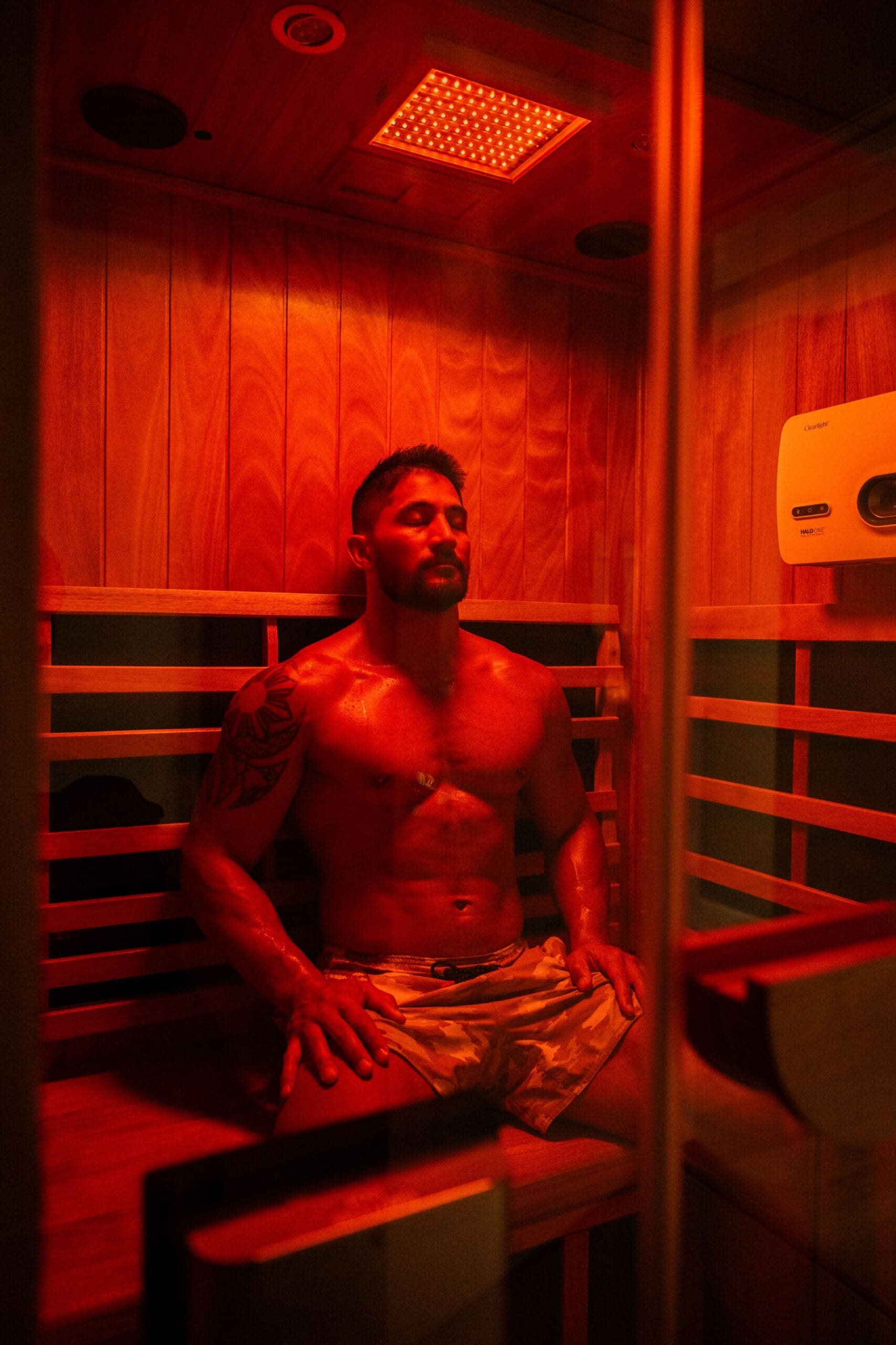 A man sits in an infrared sauna in shorts at Compass Rose Health and Wellness