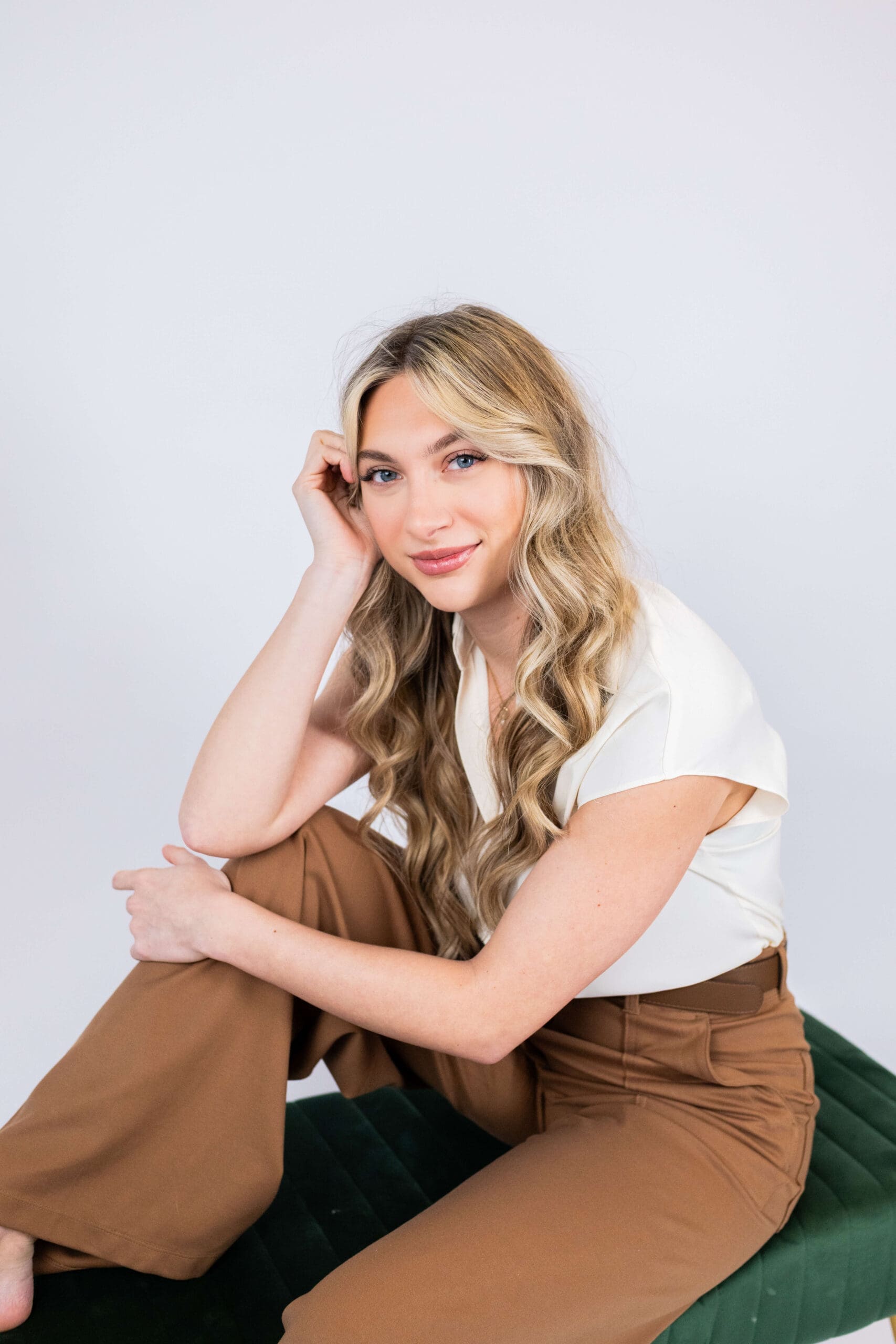 A woman in brown pants and white blouse sits across a green bench leaning on her knee after shopping at boutiques in bluffton, sc