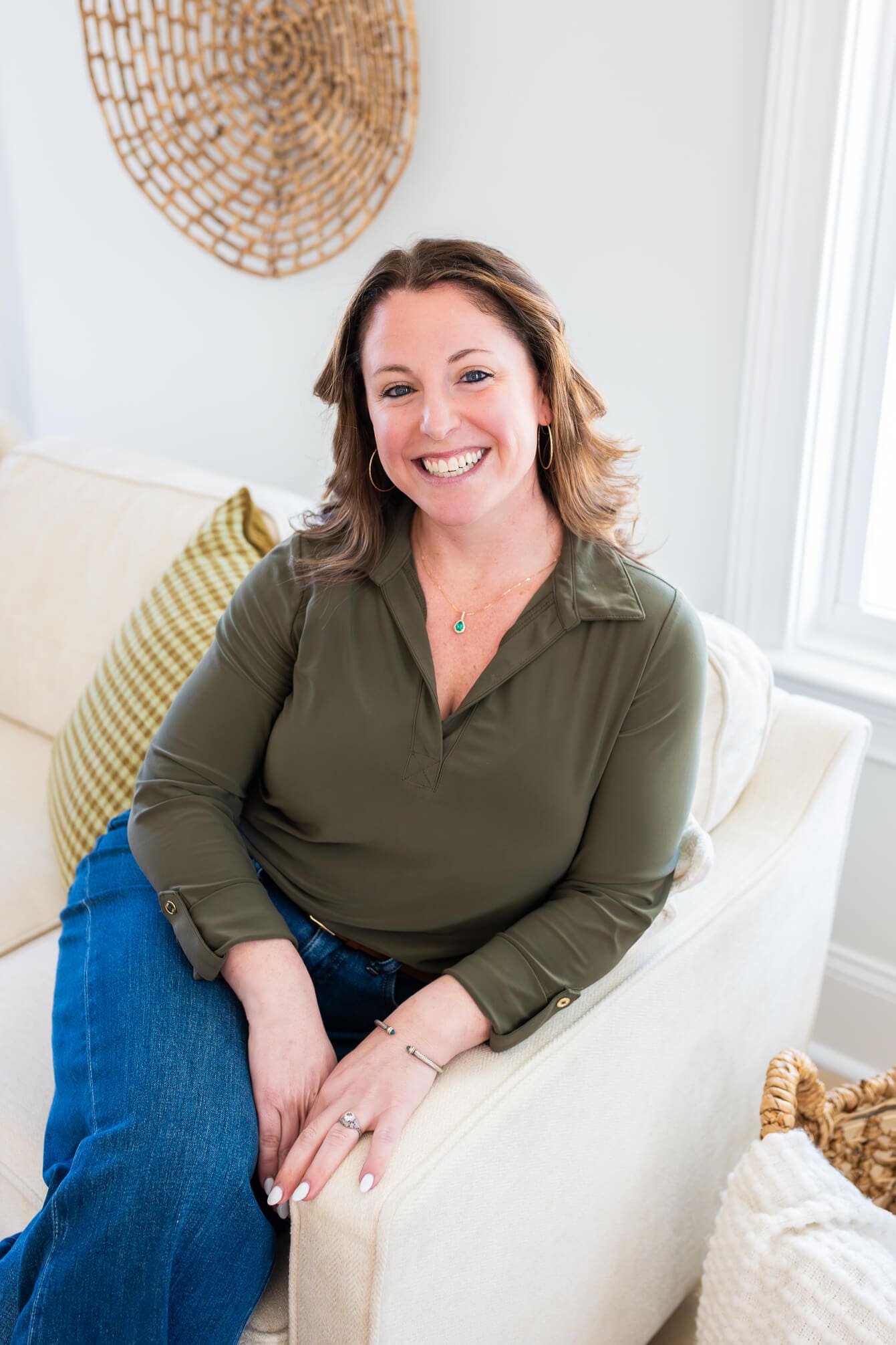 A smiling woman sits on a couch in jeans and green blouse