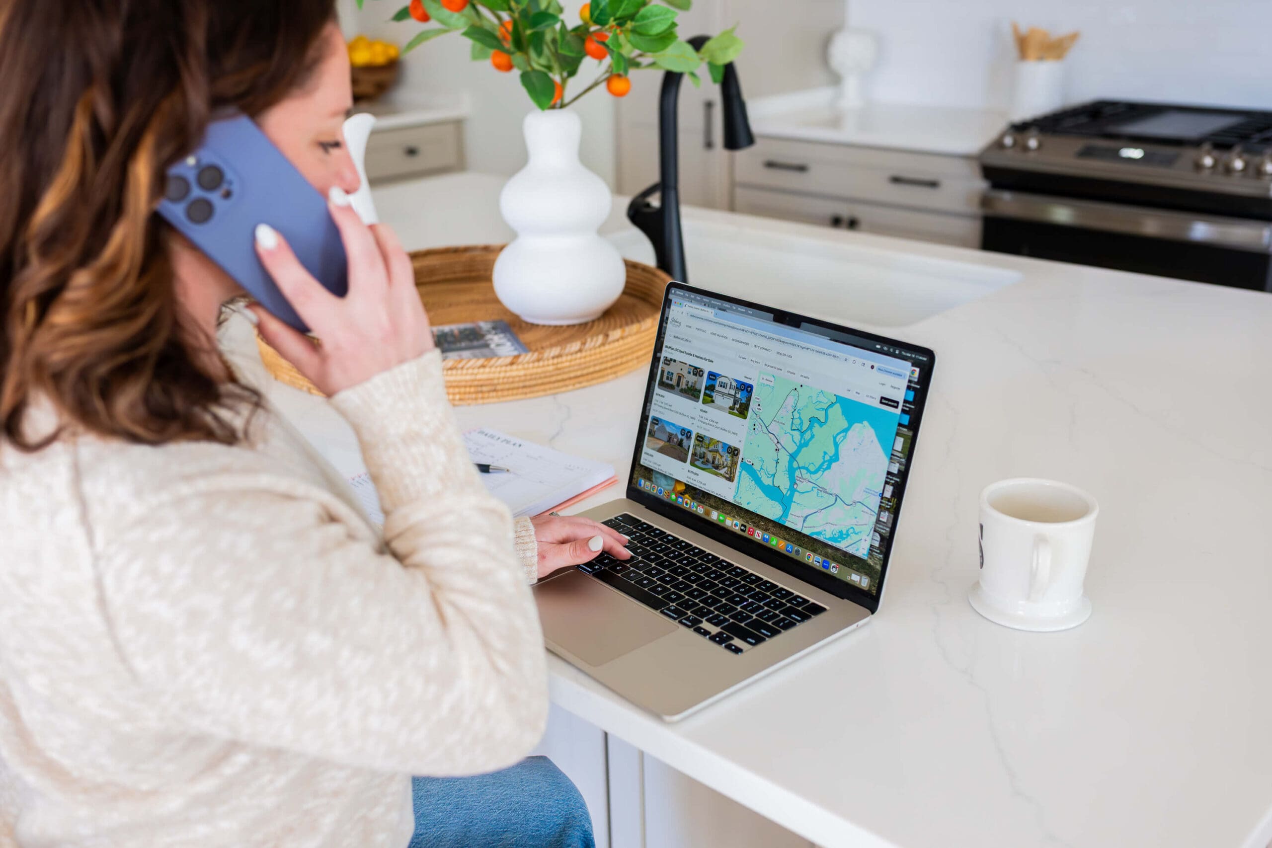 Details of a woman on the phone at a kitchen island on a laptop with a cup of coffee