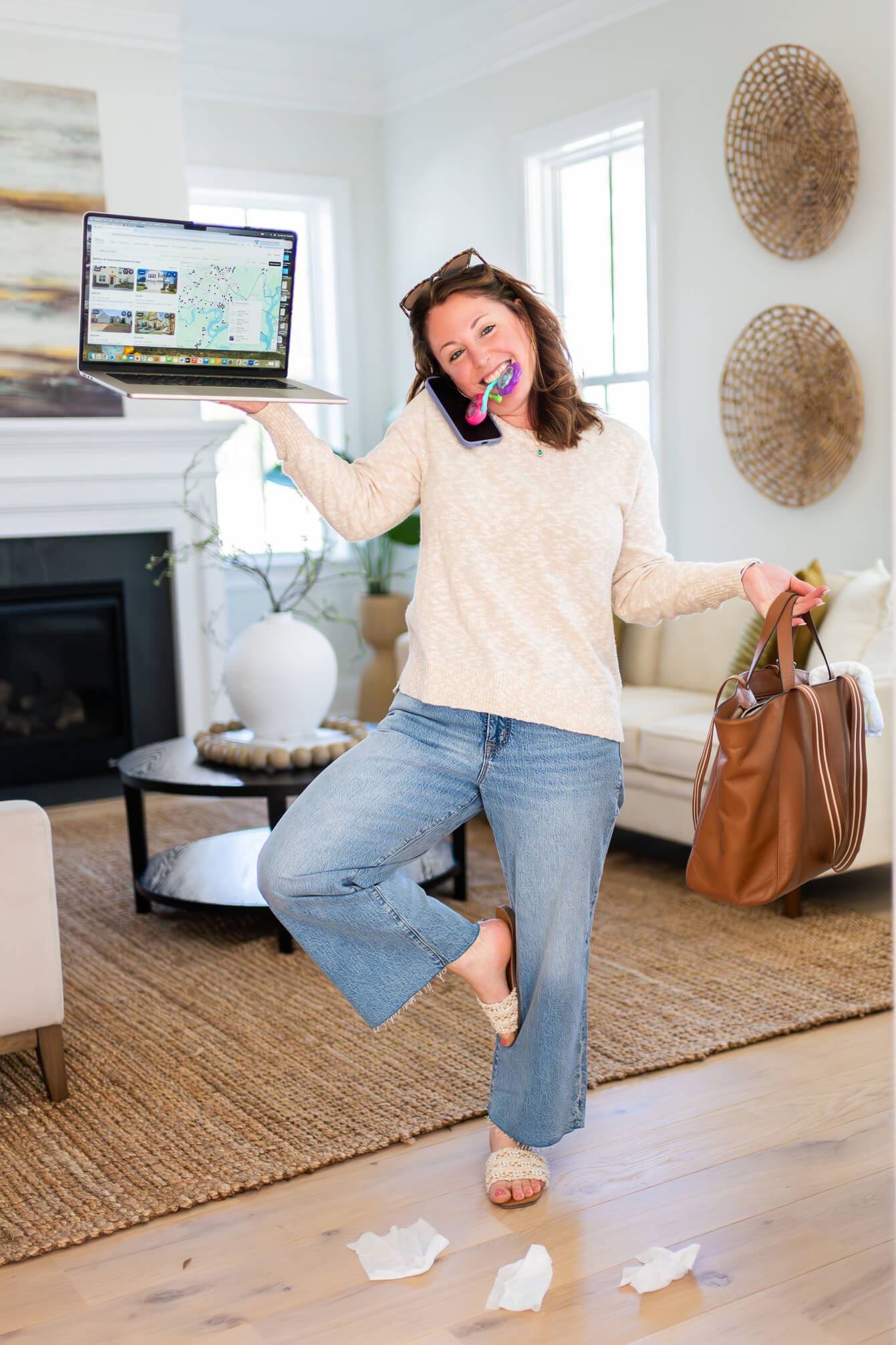 A woman stands juggling a laptop, keys and large purse in a living room for her real estate branding photos