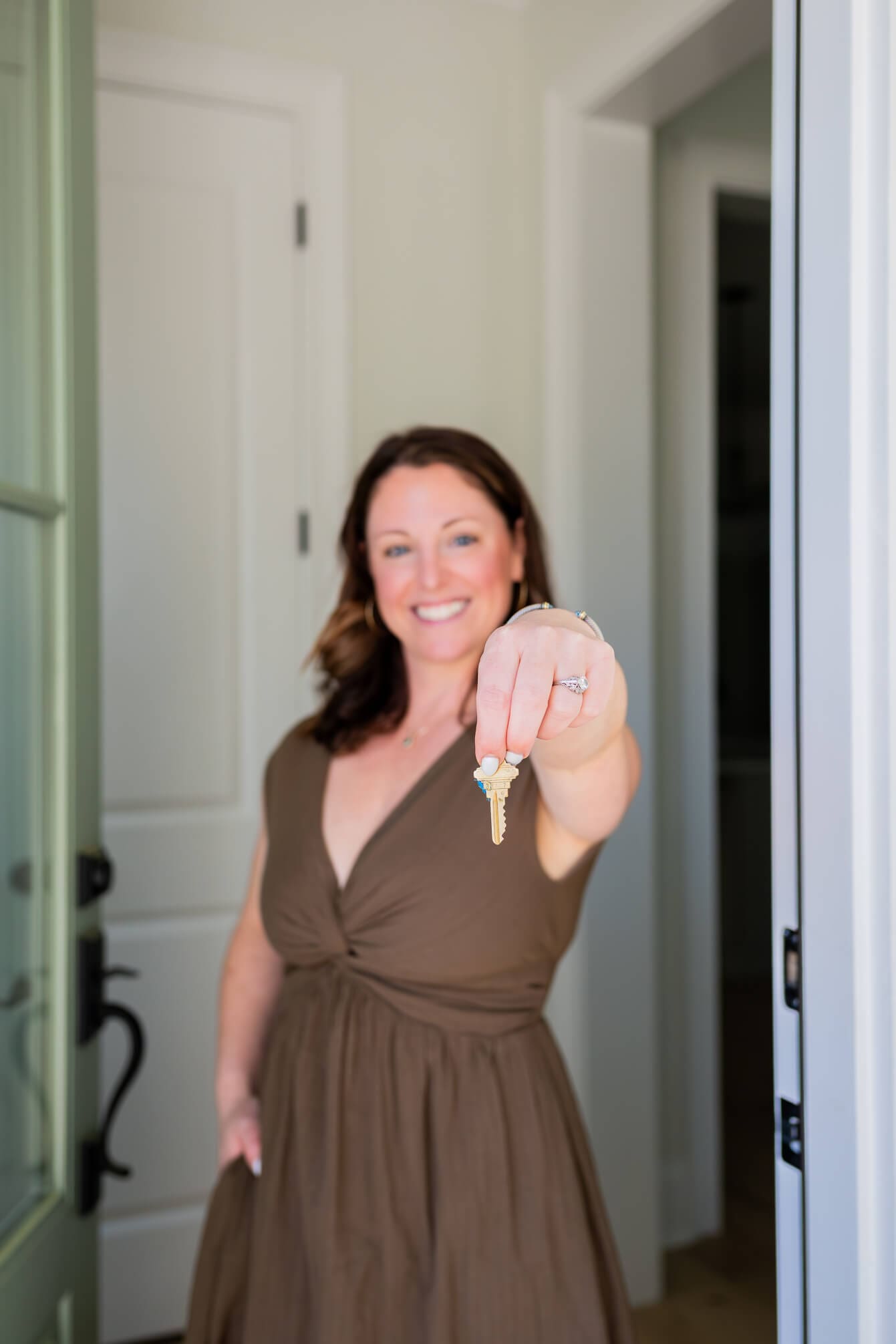 A woman stands in a doorway holding a gold key out in front of her in a brown dress