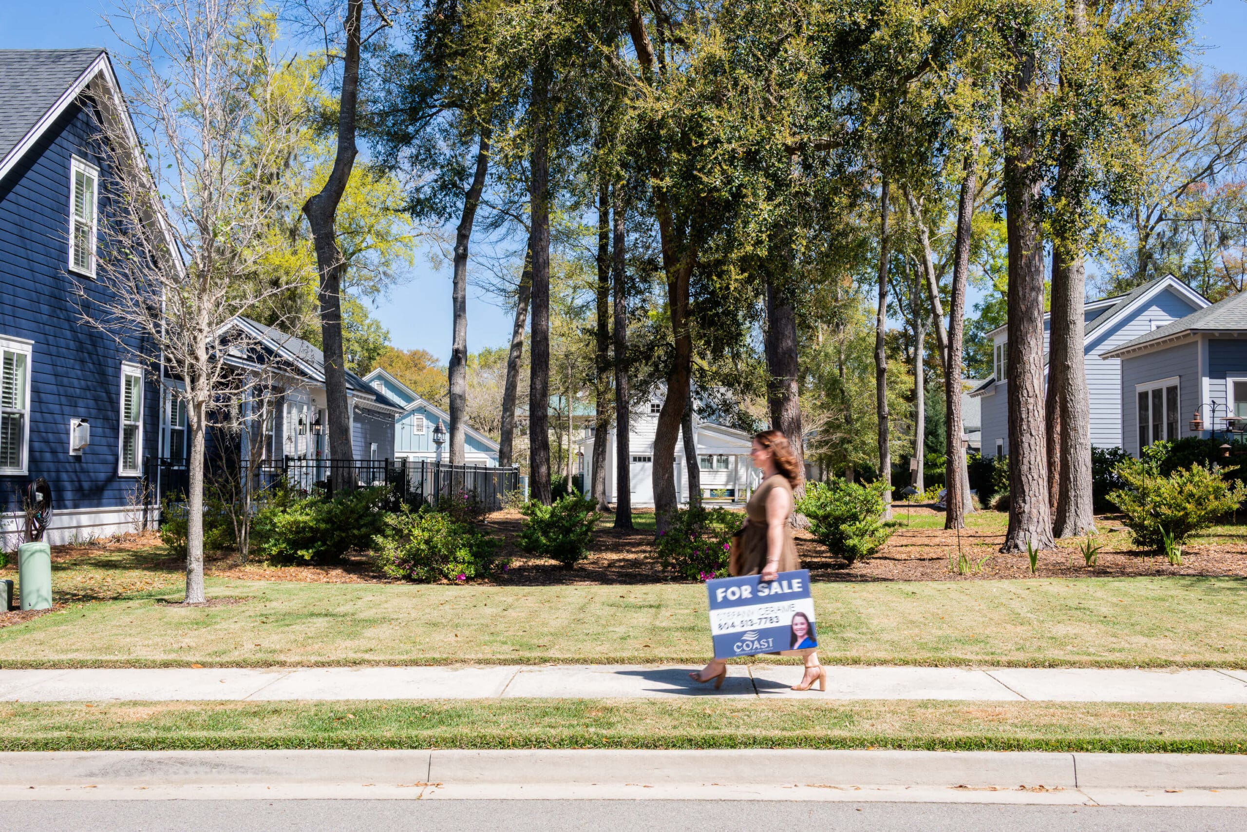 A woman walks down the street holding a for sale sign during her real estate branding photos