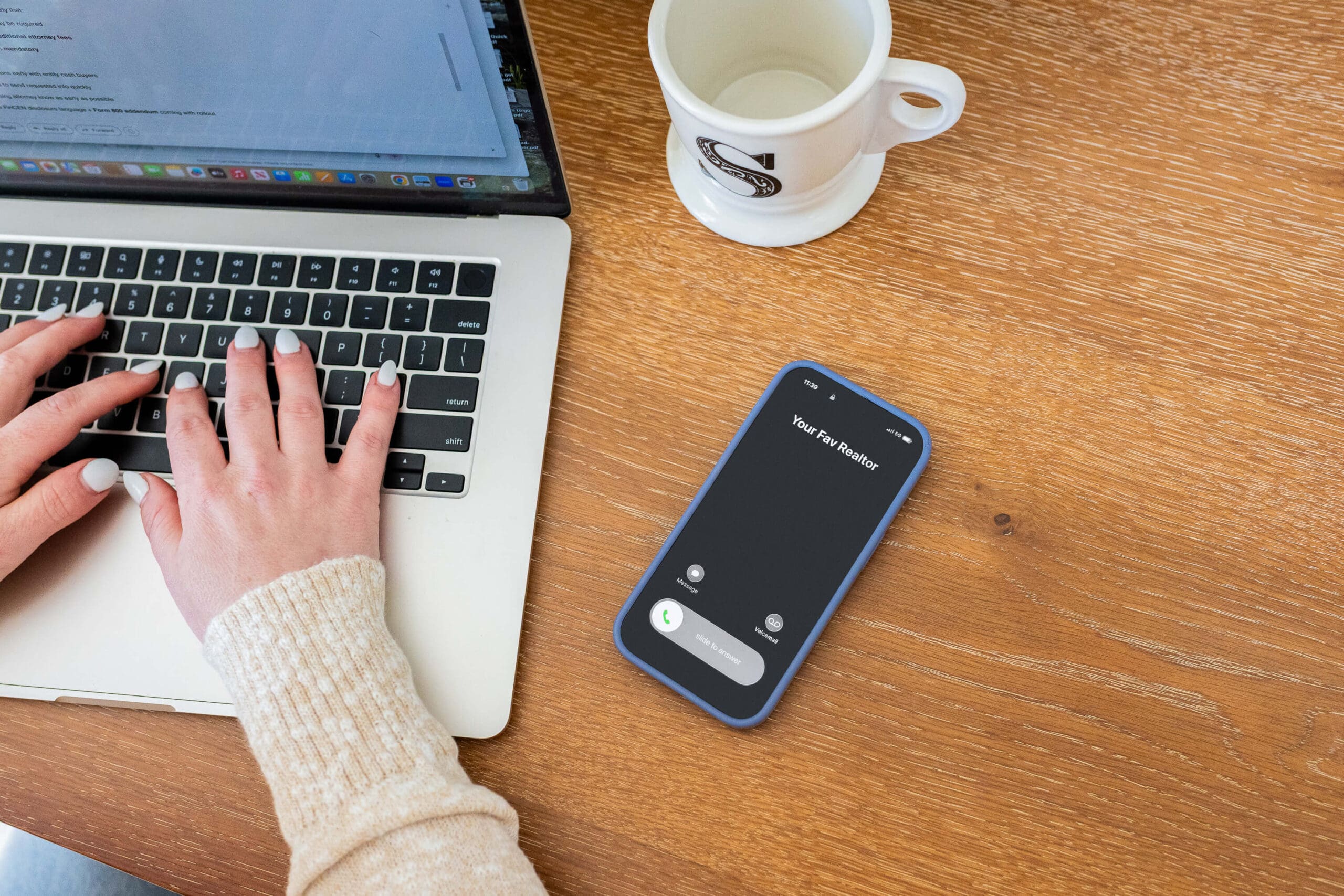 Details of a phone recieving a call on a desk with a woman at a laptop for some real estate branding photos