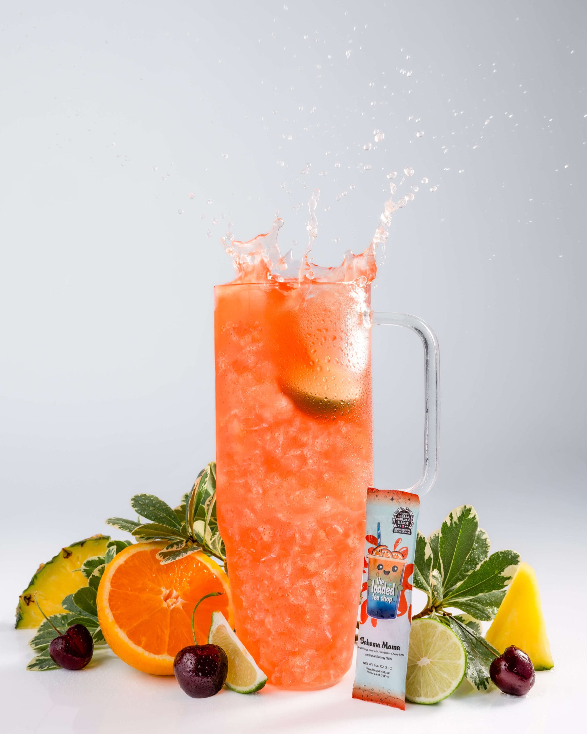 A lime splashes in an orange drink on a table with fruit and drink pouch