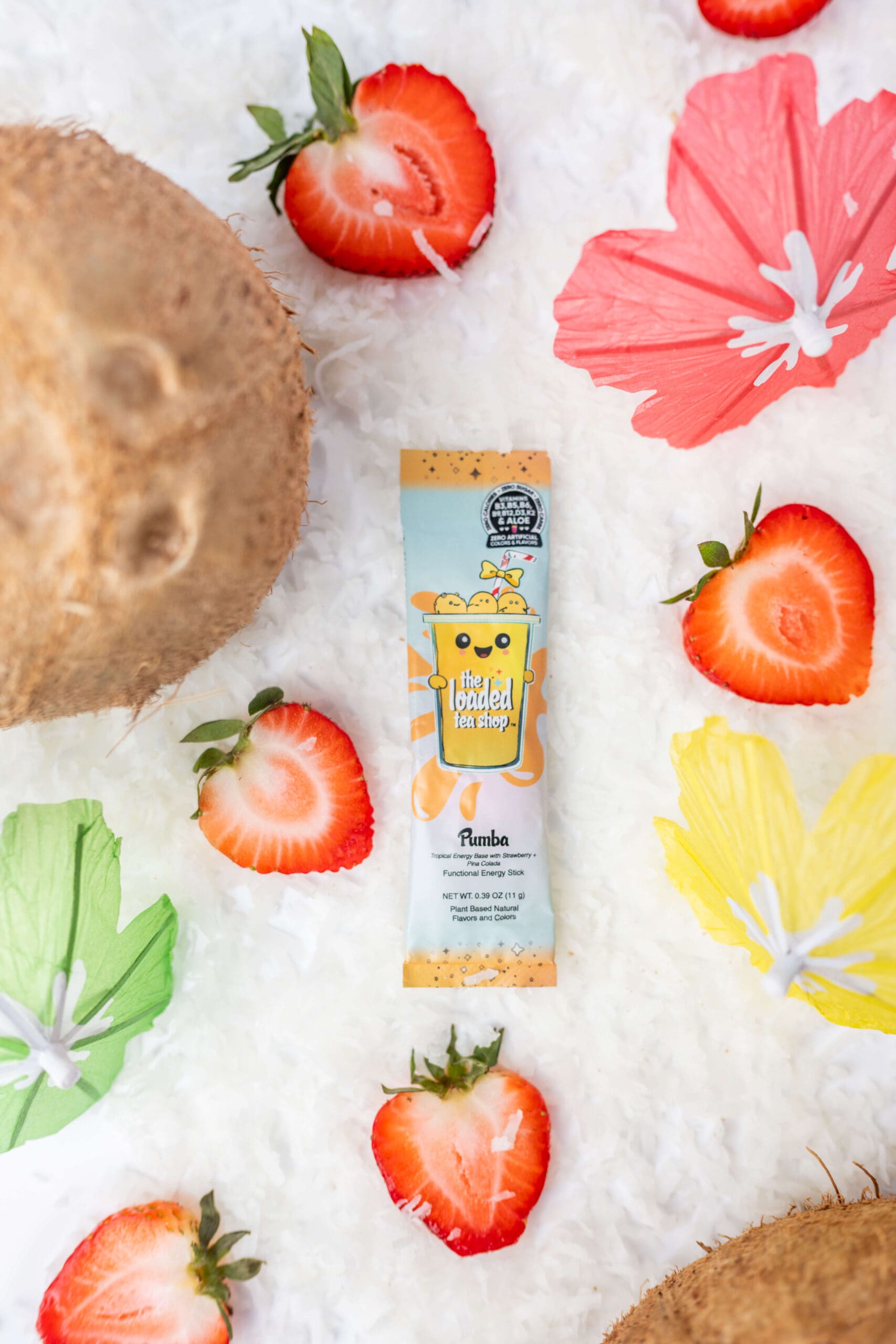 A tropical drink powder pouch lays in a bed of coconut shavings with strawberries and drink umbrellas